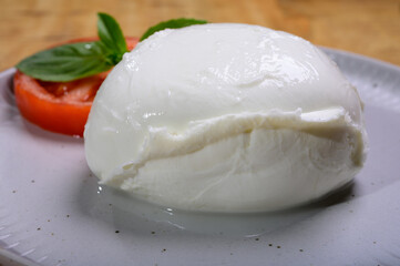 White ball of Italian soft cheese Mozzarella di Bufala Campana served with fresh green basil and red tomato