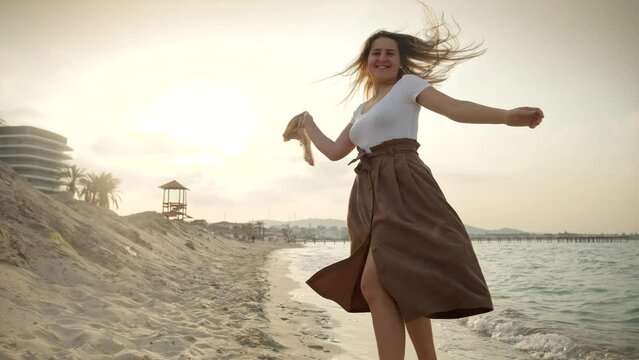Happy young woman playfully dances on the beach with a flowing silk scarf as the sun sets. Concept of joy, travel, adventure, and vacation