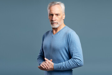 Portrait of serious senior man wearing casual sweater, looking at camera isolated on blue background