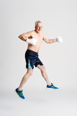 Smiling senior man in boxing gloves training isolated on white background. Male doing sports
