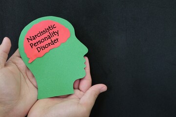 Narcissistic personality disorder help, care and treatment concept. Hand holding human head profile with word text on brain on dark background. - obrazy, fototapety, plakaty