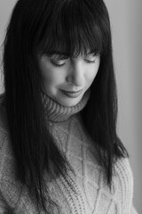 Obraz premium Black and white portrait of a 30 year old caucasian woman wearing a knitted sweater. She has dark hair and is looking downwards. Her eyes are closed.
