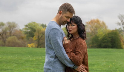 Fall portrait of an attractive caucasian couple embracing. The man is wearing a light blue long...