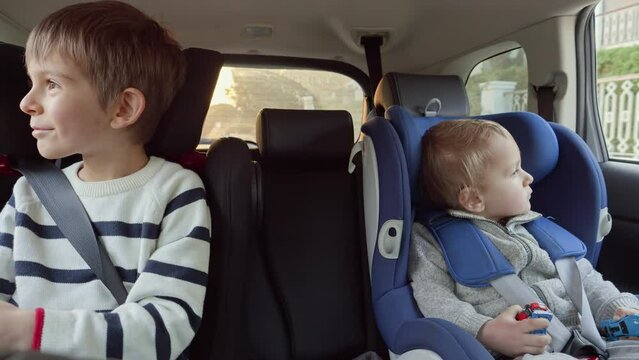 Two happy smiling kids sitting on the car back row and looking out of the window at sunset. Concept of kids traveling, baby safety, children going by car