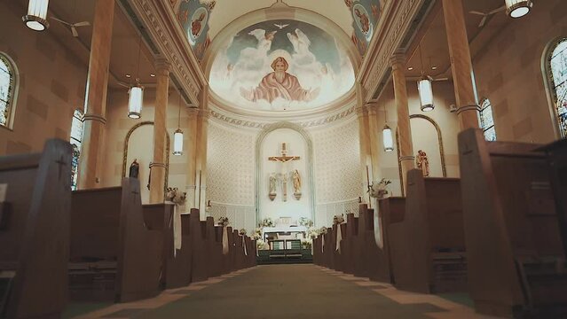 Panning down a cathedral/catholic church before mass looking at a mural of God over a crucifix.