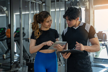 Smiling young woman and personal trainer with clipboard writing exercise plan in gym, fitness, sport, workout and diet concept