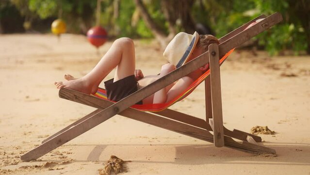 Boy Lying On Sun Lounger Using His Hat To Cover His Face