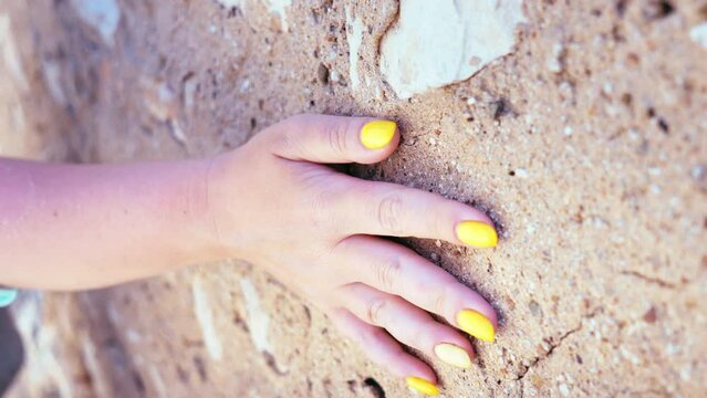 Close-up of woman's hand gliding on textured old stone wall