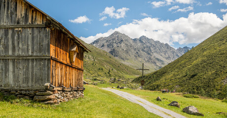 Summer alpine view of a wooden barn in a fresh alpine meadow with a hiking trail next to the barn...