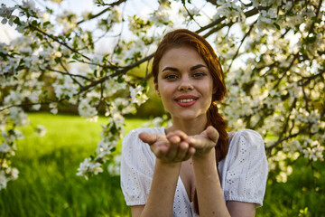 openly smiling woman against the backdrop of a flowering tree stretches her palms to the camera