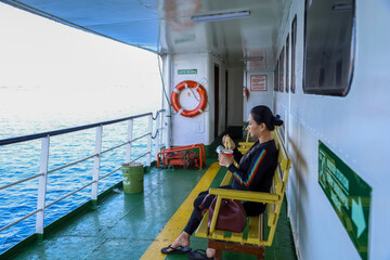asian woman eating instant cup noodles on a boat trip. Ferry passengers eat on the way at sea