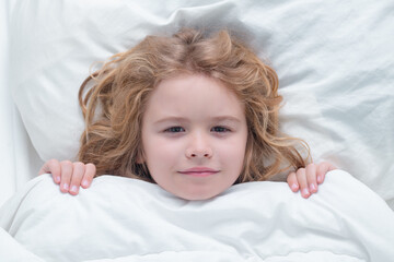 Kid under covers, face cover with blanket. Child wakes up from sleep in bed. Kid wakes up in the morning in the bedroom. Healthy sleeping, zzz concept.
