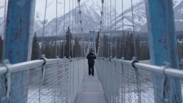 man torist walking on Siffleur Falls Trailhead hanging bridge in canadian rockies during winter