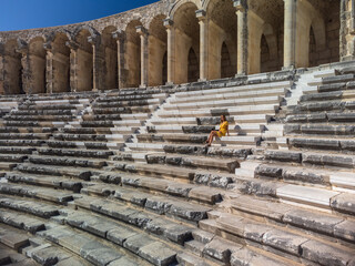 Cute woman tourist in yellow dress siting in ancient amphitheatre Aspendos 