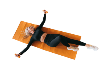 View from top on fit caucasian blonde woman in black sportswear laying on mat trains with dumbbells against transparent background looks away. Fitness and healthy lifestyle. Gym, sport.