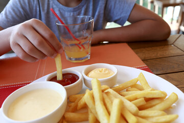 Person dipping french fries in tomato sauce