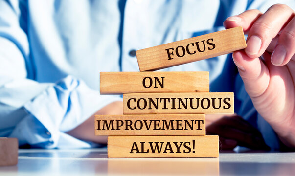 Close up on businessman holding a wooden block with a "Focus on continuous improvement always" message