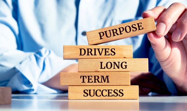 Close up on businessman holding a wooden block with a "Purpose drives long-term success" message