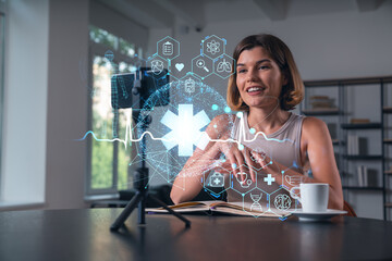 Happy woman is making video blog using smartphone on a tripod explaining with hands at office workplace. Concept of online stream, business education, conference call. Medical health care hologram