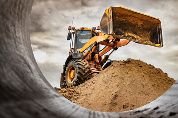 Powerful wheel loader or bulldozer working on a quarry or construction site. Loader with a full bucket of sand against the sky. Powerful modern equipment for earthworks. - obrazy, fototapety, plakaty