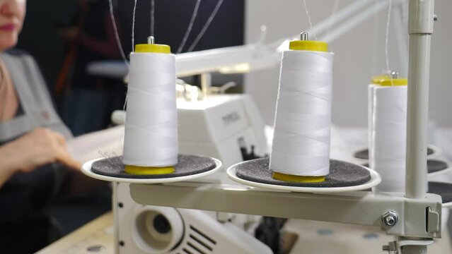 Spinning clews with thread on rack at textile plant. Thread from spool is wound onto a bobbin in sewing machine. Tailoring, thread unrolling from reel. threads spinning while sewing machine working in
