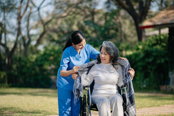 Naklejka premium Asian young caregiver nurse support senior older male walking outdoors. Specialis doctor help and take care of elderly mature. Nursing home hospital garden