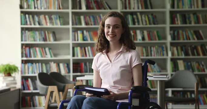 Girl smile look at camera sit in wheelchair in library, holds diary, ready for studies, feels satisfied with college admission. Human rights, accessibility in educational system people with disability