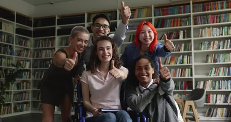 Teen girl with physical disability sit in wheelchair pose look at camera with group of cheerful multi ethnic group-mates demonstrate thumbs up, celebrate admission, showing support, amity, equality