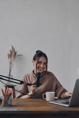 Attractive young woman looking at camera and smiling while recording podcast in studio