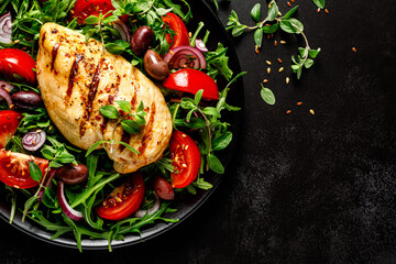 Chicken breast fillet grilled and fresh vegetable green salad with arugula, tomatoes and olives on black background, healthy food, mediterranean diet, top view - 595497117