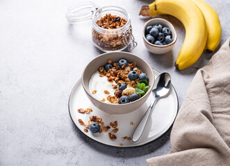 Muesli with vegetarian yogurt, banana and blueberries in a bowl on a gray texture background. Healthy and dietary homemade granola for breakfast.