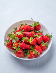 Juicy strawberries in a white bowl on a light blue background. Farm ripe healthy berries.