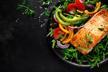 Fototapeta Salmon fillet grilled and fresh vegetable green salad of arugula with tomatoes, olives and bell pepper on black background, healthy food, mediterranean diet, top view obraz