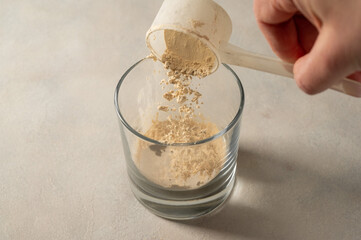 Pouring protein powder from scoop, in glass a glass. Making protein drink.