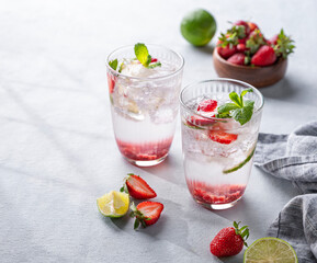 Fresh strawberry mojito in a glass with berries, lime, mint and ice on a light background with shadow. The concept of a summer refreshing drink for a party.