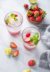 Fresh strawberry mojito in a glass with berries, lime, mint and ice on a light background with shadow. The concept of a summer refreshing drink for a party