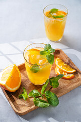 Naklejka na ściany i meble Orange juice with fresh fruits, mint and ice on a light background with shadow. Healthy freshly squeezed citrus detox drink for breakfast.