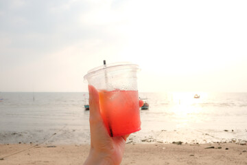 Hand holding strawberry lemon soda in take away cup (plastic glass) on the beach background.