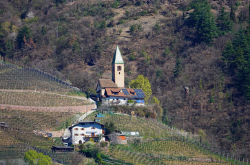 Teleaufnahme einer Kirche an einem Berghang in Südtirol, umgeben von Wiesen und Bäumen