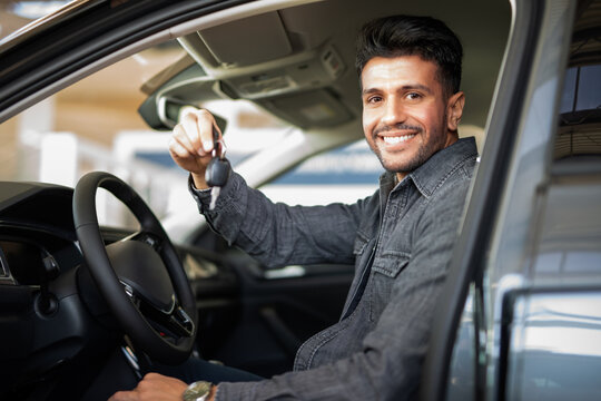 Man showing the key of his new car in a car dealer saloon