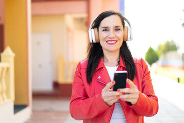 Middle aged woman listening music with a mobile and looking front