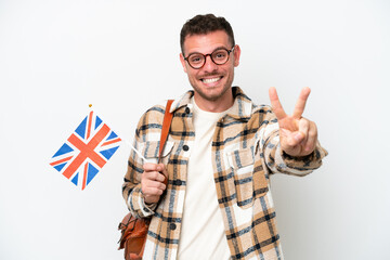 Young hispanic man holding an United Kingdom flag isolated on white background smiling and showing victory sign