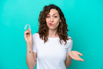 Young caucasian woman holding a envisaging isolated on blue background making doubts gesture while lifting the shoulders