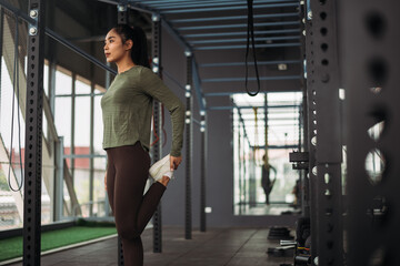Fototapeta na wymiar Strong asian woman streching body before exercise at crossfit gym. Athlete female wearing sportswear warm-up before workout on grey gym background with weight and dumbbell equipment.