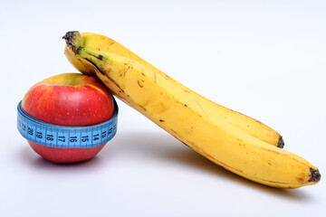 Dojrzały żółty banan oparty o czerwone jablko owinięte taśma mierniczą, centymetr krawiecki...