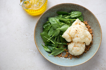 Plate with steamed cauliflower cabbage and fresh spinach, horizontal shot on a light-beige stone background, elevated view