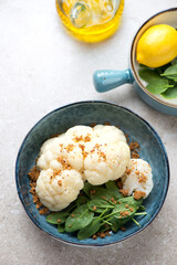 Steamed cauliflower with fresh spinach and bread crumbs served in a blue bowl, vertical shot on a beige stone background