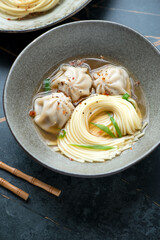 Bowl of wonton soup with egg noodles, vertical shot on a dark-olive marble background, vertical shot