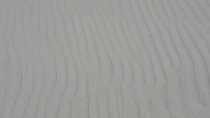 White sand dune with ripples and wisps of sand being blown off the crest.