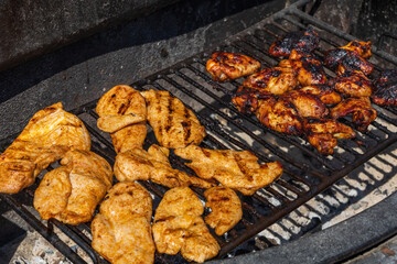 Chicken breasts and chicken wings are marinated and grilled on an outdoor grill.